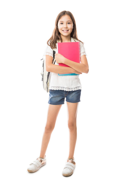 Portrait of smiling schoolgirl with school bag on back holding books isolated on white background - Foto, Imagen