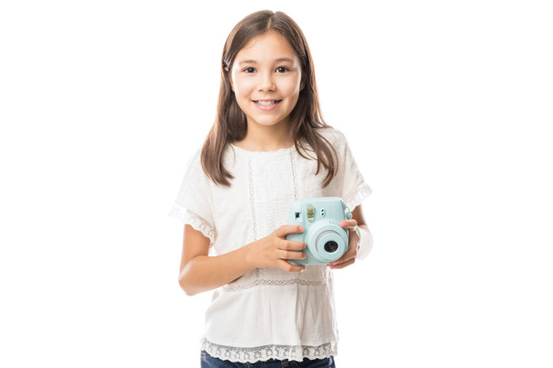 Smiling young girl holding photo camera and taking pictures isolated on white background - Photo, Image