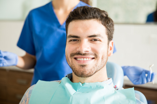 Ritratto di uomo adulto sorridente con dentista che tiene strumenti dentali in clinica
 - Foto, immagini