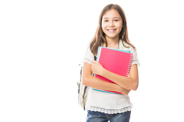 Portrait of smiling schoolgirl with school bag on back holding books isolated on white background - Photo, Image