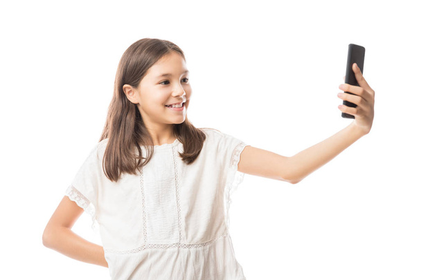 Schattige lachende meisje in witte blouse selfie met smartphone geïsoleerd op witte achtergrond - Foto, afbeelding