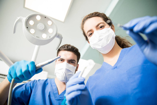Erkek ve kadın diş hekimleri diş kliniğinde çalışırken maskeli düşük açılı portresi - Fotoğraf, Görsel