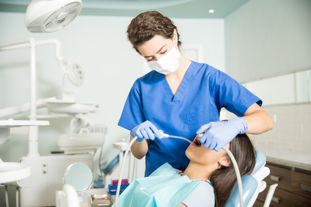 Kobieta dentysty przy użyciu Ślinociąg i dentystyczny wiertło podczas leczenia nastolatkę w klinice - Zdjęcie, obraz