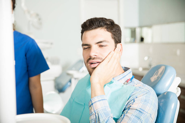 歯科医院で歯科医によって坐っている間歯痛で苦しんでいる 30 代の男性 - 写真・画像