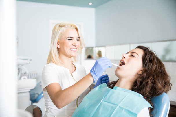 Szczęśliwa kobieta dentysty robi sprawdzanie i czyszczenie w ustach pacjenta w klinice stomatologicznej - Zdjęcie, obraz