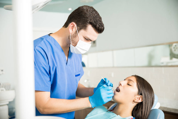 Férfi fogorvos vizsgáló tizenéves lány fogorvosi tükörrel és carver klinikán - Fotó, kép