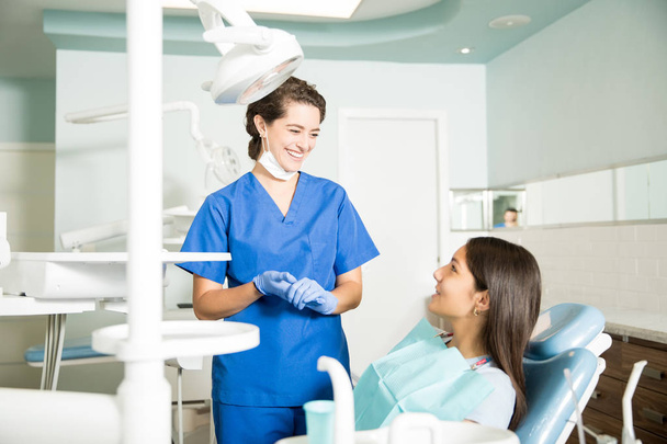 Χαμογελαστά γυναικεία οδοντίατρος στην ομοιόμορφη μιλάμε για εφηβικό κορίτσι στο οδοντιατρείο - Φωτογραφία, εικόνα