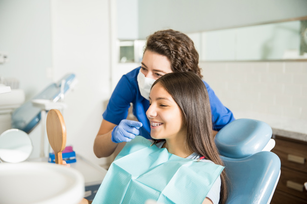 Zahnärztin zeigt Teenagerin in Zahnklinik Zahnspange im Spiegel - Foto, Bild