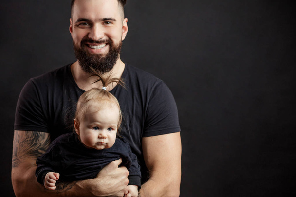 Young athletic father with adorable baby on black background - Fotografie, Obrázek
