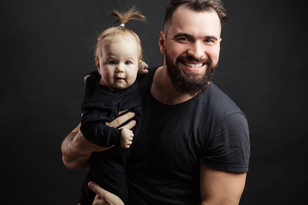 Young athletic father with adorable baby on black background - Foto, afbeelding