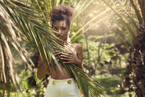 Tropical shoot of beautiful african american woman wearing earring, posing over palm leaves. - Fotó, kép