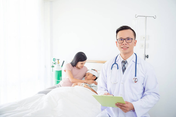 schöner asiatischer Arzt lächelt vor die Kamera mit Patient und Familie im Hintergrund - Foto, Bild