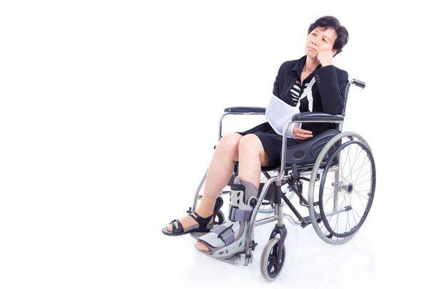 Азиатская бизнесвумен со сломанной рукой и ногой сидит в инвалидном кресле на белом фоне
 - Фото, изображение