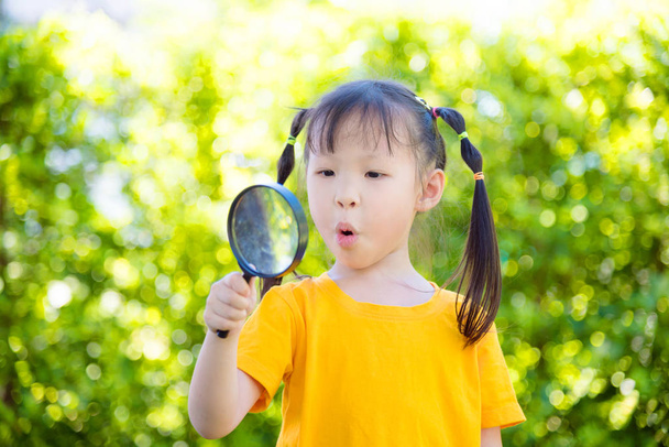 kleine asiatische Mädchen suchen durch Vergrößerung mit überrascht Gesicht in Park - Foto, Bild