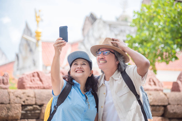 Ευτυχισμένος/η Ασιάτης/ισσα συνταξιούχος ζευγάρι παίρνει τη φωτογραφία από έξυπνο τηλέφωνο σε έναν ναό στην Ταϊλάνδη - Φωτογραφία, εικόνα
