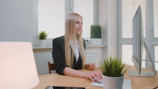 Woman showing thumbs down in office. Sitting at workplace young blond female in business suit looking at camera and doing thumbs down gesture of disapproval or dislike. - Felvétel, videó