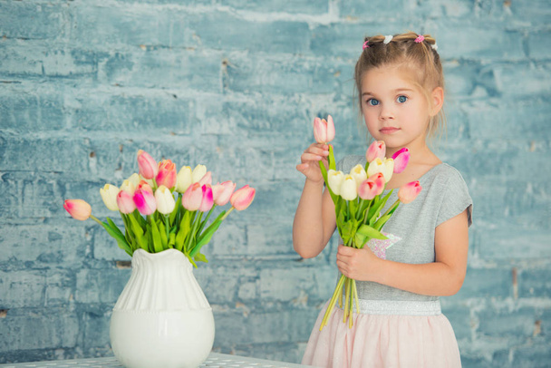 Adorable smiling little girl with tulips by the window - Foto, immagini