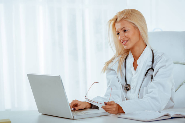 junge Ärztin schreibt auf Laptop und checkt Krankenakte im Sprechzimmer. - Foto, Bild