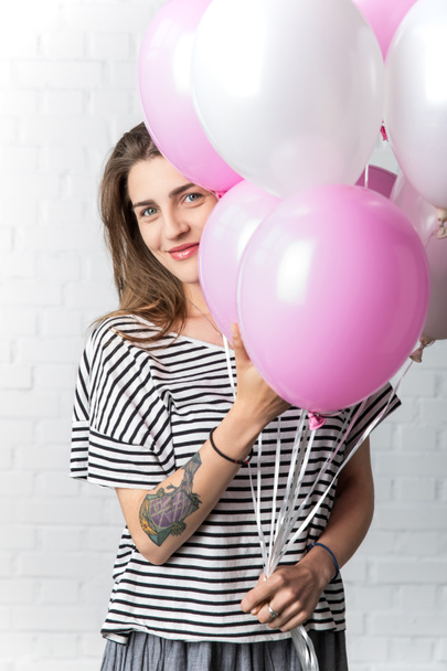 Счастливая девушка держит кучу шариков на белом кирпичном фоне стены
 - Фото, изображение