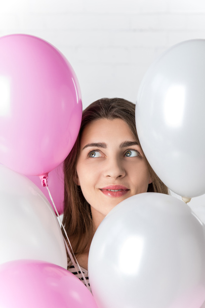 Usmívající se dívka mezi balónky na pozadí bílá cihlová zeď - Fotografie, Obrázek