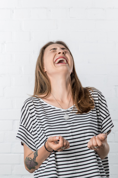 Сміється молода жінка в смугастій сорочці на фоні білої цегляної стіни
 - Фото, зображення