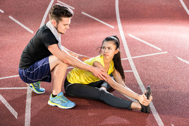 Man and woman on cinder track of sports arena stretching exercises - Photo, Image