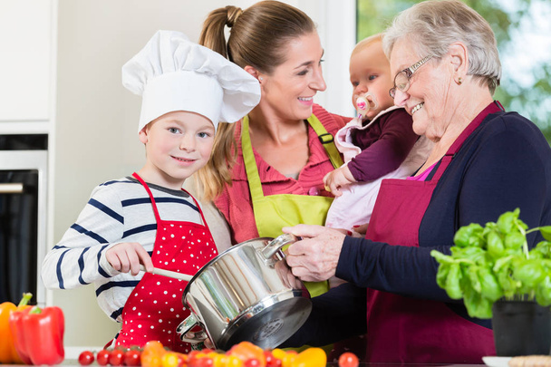 Mom, dad, granny and grandson together in kitchen preparing food - Photo, Image