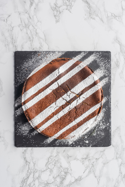top view of delicious homemade cake with icing on slate board on marble surface - Photo, Image