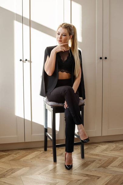Portrait of beauty blonde woman in black casual clothes sitting on wooden chair in luxury room interior  - Fotoğraf, Görsel