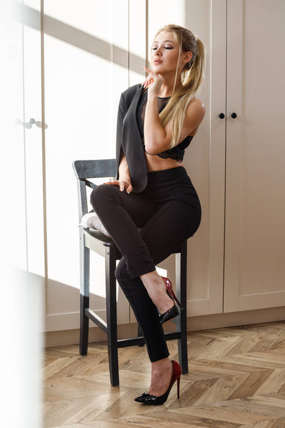 Portrait of beauty blonde woman in black casual clothes sitting on wooden chair in luxury room interior  - Foto, Imagem