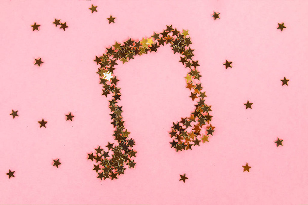Musical notes of starry golden confetti lying on a pink pastel background - Фото, зображення