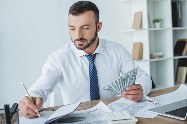 handsome business adviser counting money in office and writing something to notebook - Photo, Image