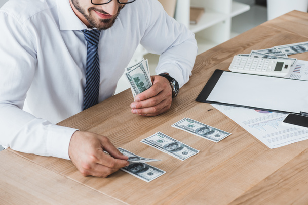 imagen recortada del asesor de negocios contando billetes de dólar en la mesa en la oficina
 - Foto, Imagen