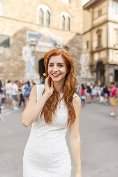 Attractive redhead woman in white dress posing on street of Florence - Photo, image