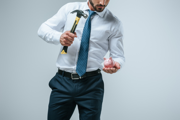 обрезанное изображение финансиста, разбивающего копилку молотком, изолированным на сером
 - Фото, изображение