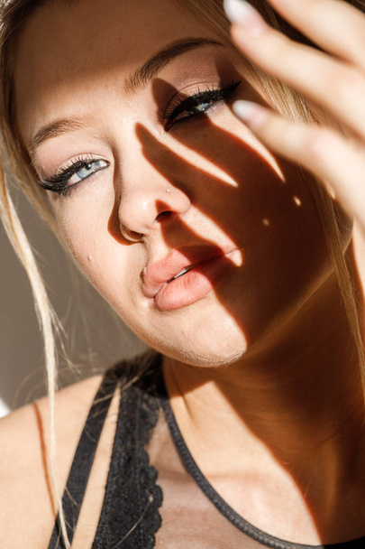 Closeup portrait of beautiful blonde girl in black clothes sitting on floor. Shot of sensual woman with shadow on face  - Fotoğraf, Görsel