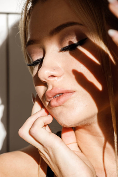 Closeup portrait of beautiful blonde girl in black clothes sitting on floor. Shot of sensual woman with shadow on face  - Foto, Imagem