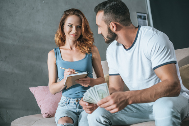 happy couple planning family budget and counting money in living room - Photo, Image