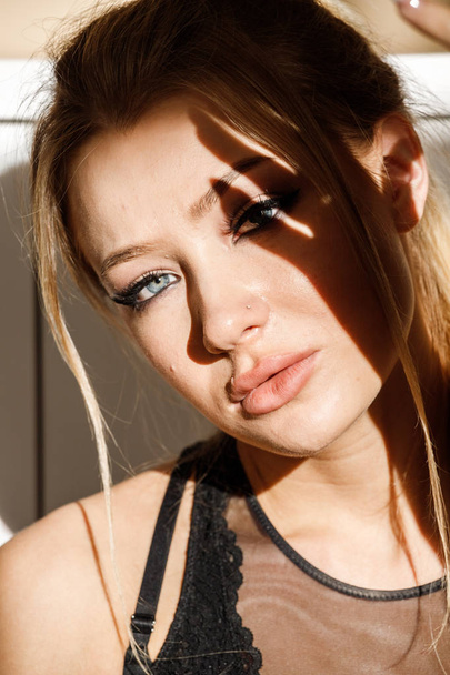 Closeup portrait of beautiful blonde girl in black clothes sitting on floor. Shot of sensual woman with shadow on face  - Valokuva, kuva