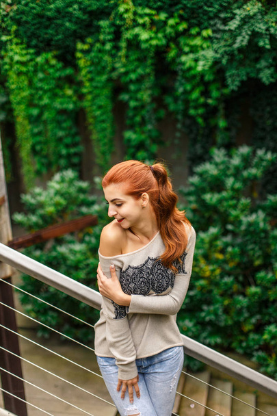 Attractive redhead woman posing on balcony before green hedge - Фото, зображення