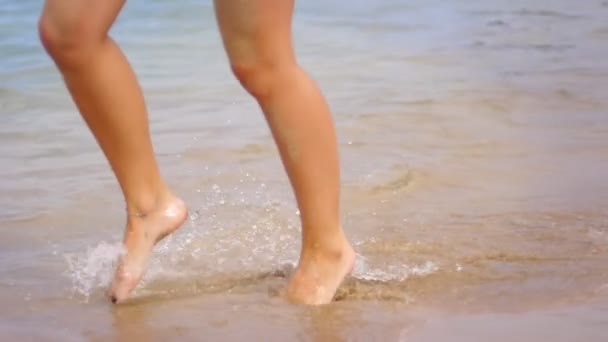 水の波の上を歩く女の子の脚。海岸で実行されている完璧な女性の足 - 映像、動画
