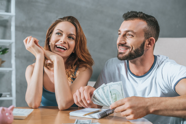 smiling couple planning family budget and looking away in living room - Фото, изображение