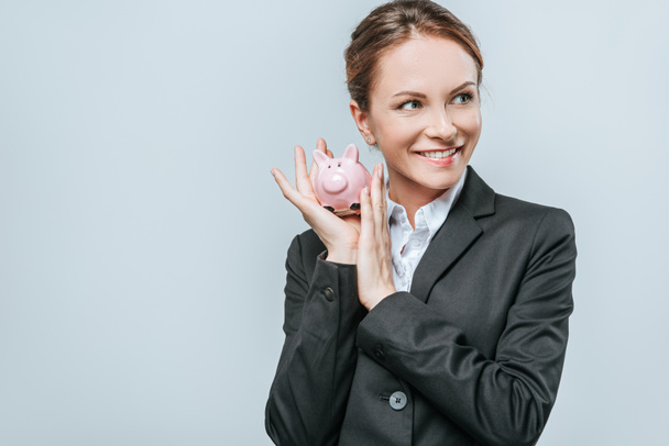 financiador sorrindo segurando porquinho banco e olhando para longe isolado em cinza
 - Foto, Imagem