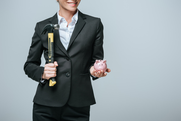 περικομμένη εικόνα χρηματοδότης κρατάει σφυρί και κουμπαράς απομονωμένος σε γκρι - Φωτογραφία, εικόνα