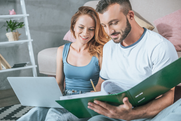 happy couple planning family budget in living room with laptop and folder - Foto, Imagen