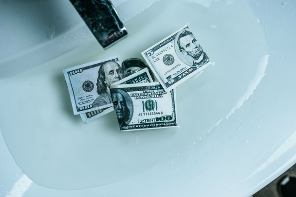 verhoogde weergave van dollar biljetten in water in wastafel - Foto, afbeelding