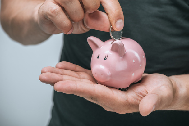 cropped image of man putting coin in pink piggybank isolated on grey - Photo, Image