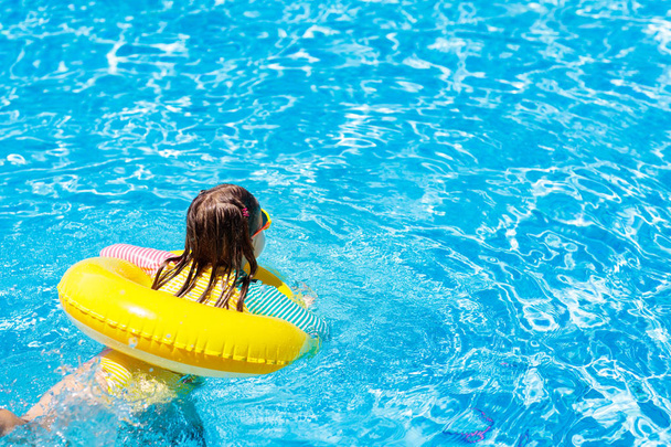 Child with sunglasses in swimming pool. Little girl on inflatable ring. Kid with yellow float. Kids learn to swim in outdoor pool of tropical resort. Sun protection and eye wear. Space for your text. - Fotoğraf, Görsel