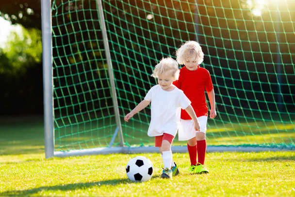 A gyerekek a szabadtéri pályán fociznak. A gyerekek gólt rúgnak a focimeccsen. A kisfiú rúgja a labdát. Futó gyerek mezben és stopliban. Iskolai foci klub. Sportoktatás fiatal játékosok számára. - Fotó, kép