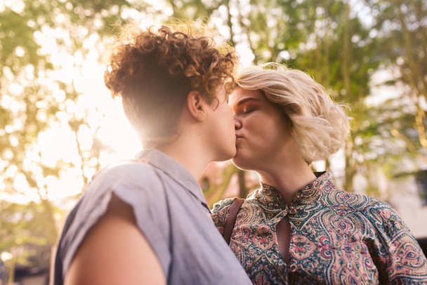 Affectionate young lesbian couple standing on a city street and kissing while enjoying a sunny day out together - Foto, Imagen